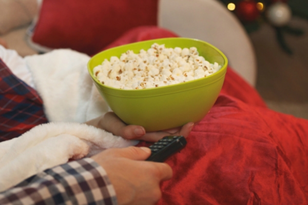 Couple on sofa with tree in background with popcorn while watching tv