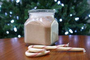 jar of homemade hot chocolate mix in front of Christmas tree with candy canes