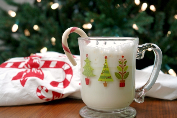 peppermint white hot chocolate in christmas mug with candy cane in front of christmas tree.