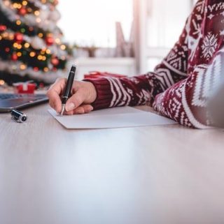 person writing on paper with christmas tree in background