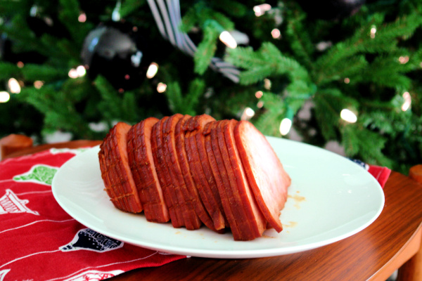 sliced ham on white plate in front of Christmas tree