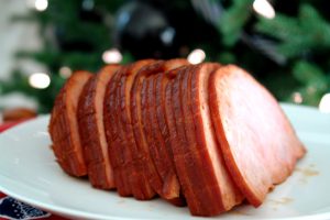 sliced ham on white plate in front of Christmas tree up close