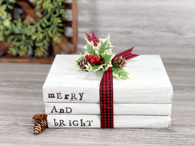 white books in stack with christmas ribbon and holly on table
