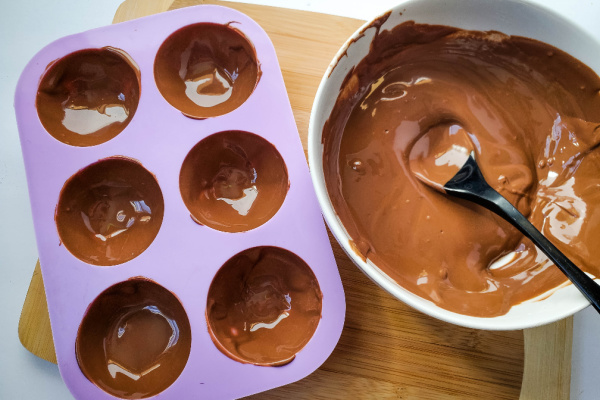 silicone mold filled with melted chocolate next to bowl of melted chocolate