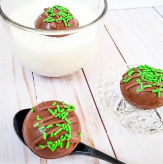 Irish cream hot chocolate bomb in glass of milk with two more sitting on table