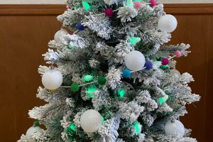 flocked christmas tree with green lights, white ornaments and rainbow garland