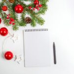 white table with christmas greenery and red ornaments with notebook and pen