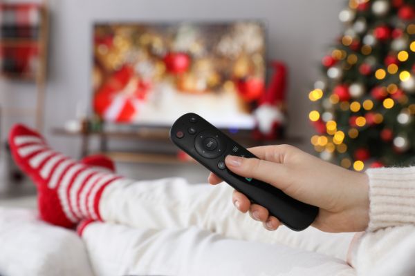 person in christmas socks pointing remote at tv playing christmas movies
