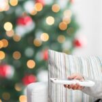 person pointing remote at tv with christmas tree in background