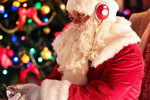 santa sitting in front of a Christmas tree listening to Christmas music with headphones and an smartphone