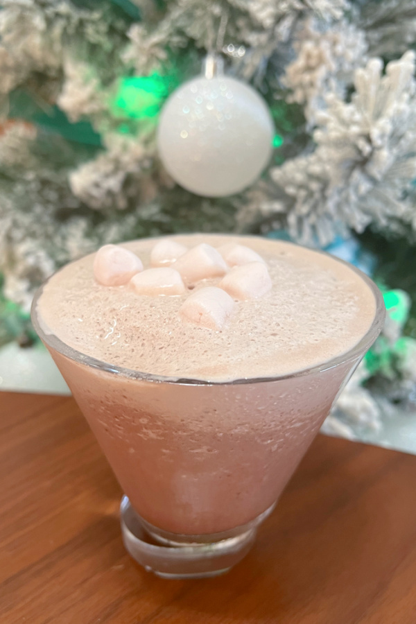 frozen hot chocolate martini in martini glass with mini marshmallows on top in front of flocked christmas tree