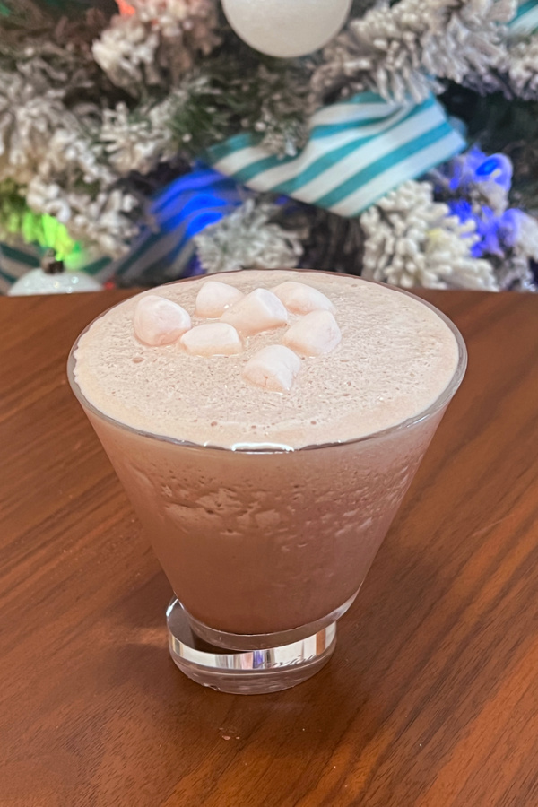 frozen hot chocolate martini in martini glass with mini marshmallows on top in front of flocked christmas tree