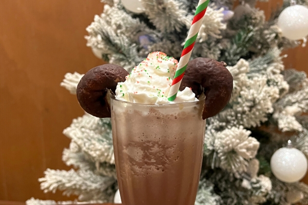 Frozen hot chocolate in glass with whipped cream, sprinkles and mini chocolate donuts that look like Mickey ears in front of a Christmas tree