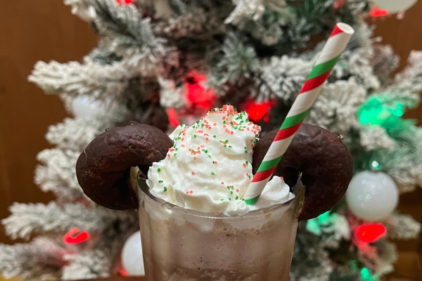 Frozen hot chocolate in glass with whipped cream, sprinkles and mini chocolate donuts that look like Mickey ears in front of a Christmas tree