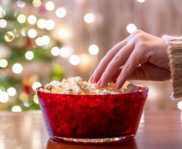 woman's hand reaching in bowl for popcorn with christmas tree in background