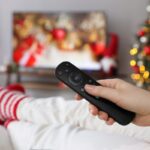 person wearing christmas socks watching christmas movies while holding remote