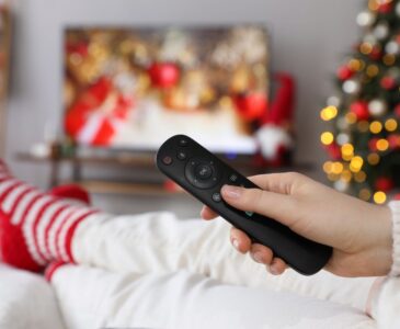 person wearing christmas socks watching christmas movies while holding remote