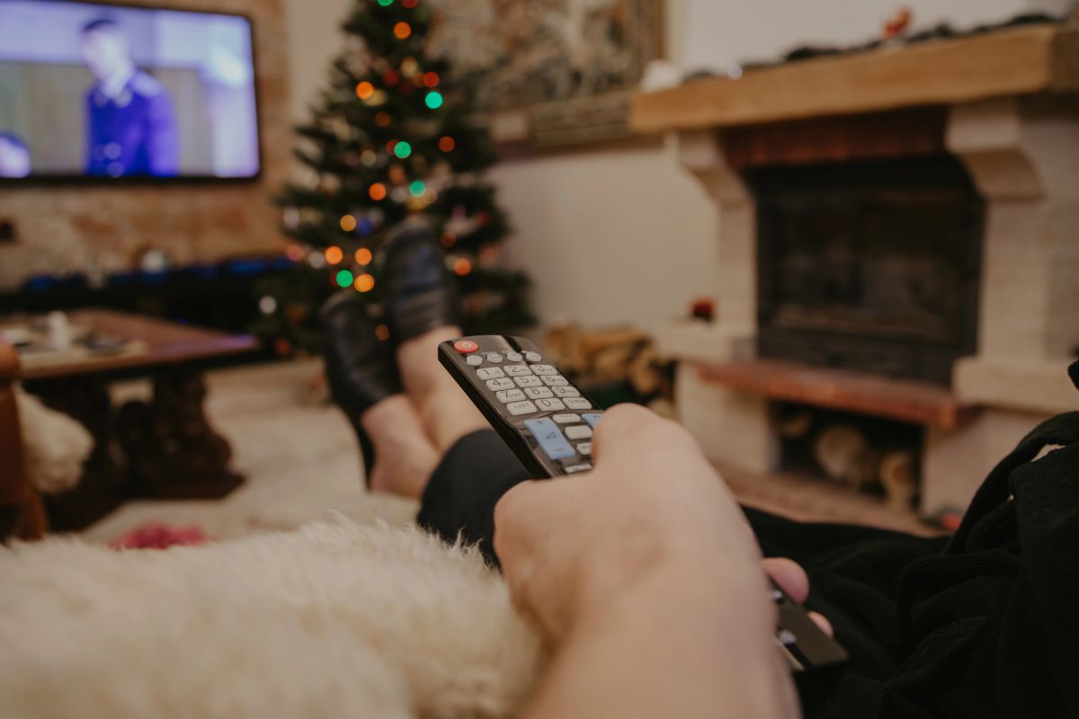 person sitting on sofa with remote in hand and christmas tree in corner of room