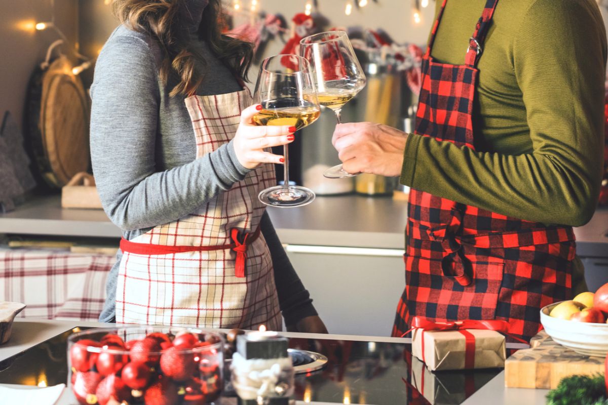 couple in kitchen with glasses of wine in christmas aprons